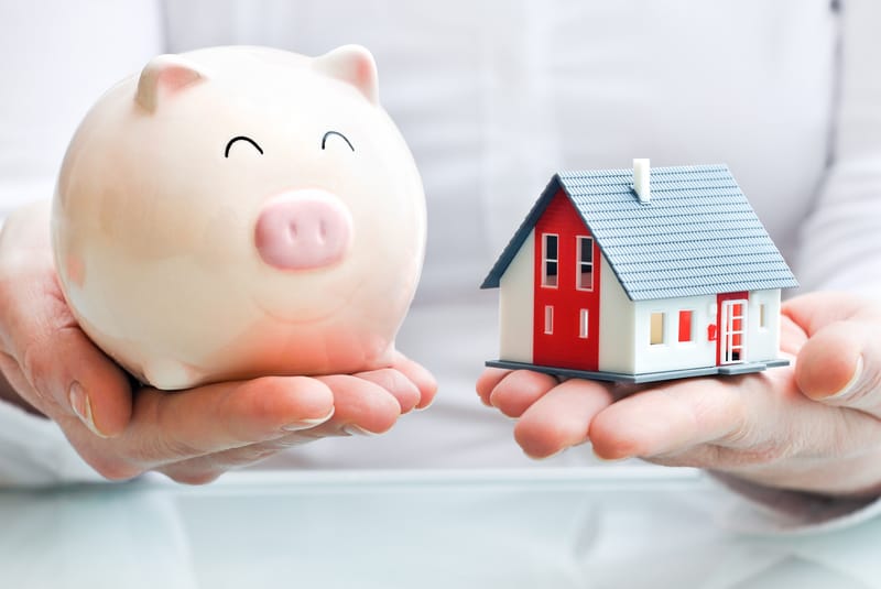 A person holding a piggy bank as well as a house in his hands